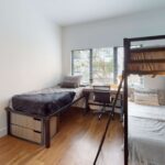 Bedroom with large window, bed, under-bed dressers, desks, desk chairs, and bunk bed
