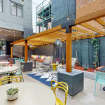 Allston Place courtyard with wood pergola, hanging lights, patio tables, chairs, and benches