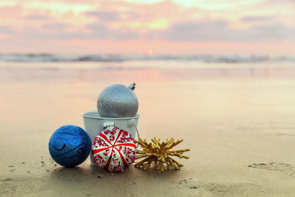 A small bucket of holiday ornaments on the beach